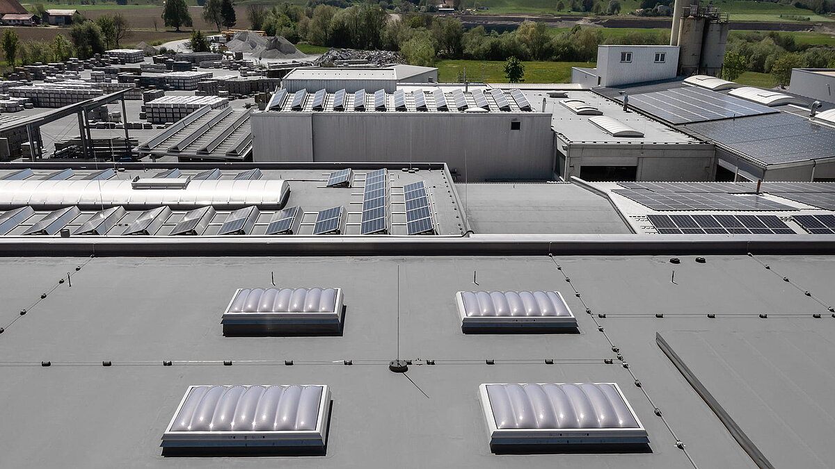 Dachansicht der Produktionshalle des Bauunternehmens Unglehrt mit LAMILUX Lichtkuppeln F100 W, Lichtbändern B und Solarpaneelen.