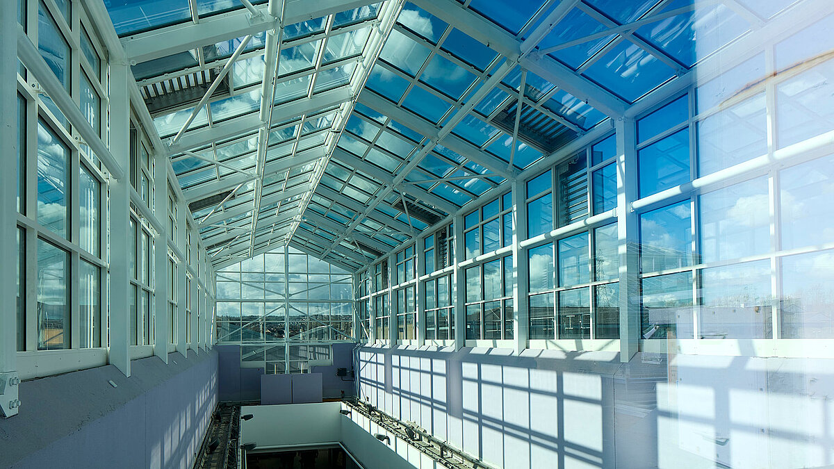 Innenansicht eines großen Glasdachs mit Stahlrahmen und Glaswänden in einem modernen Gebäude