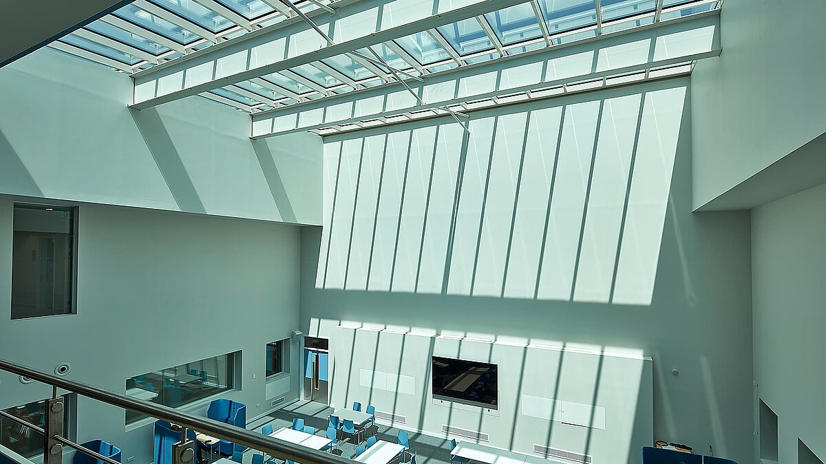 Innenansicht eines modernen Gebäudes in Milton Park, England, mit großem Glasdach, das Sonnenlicht auf die weißen Wände des Atriums wirft.