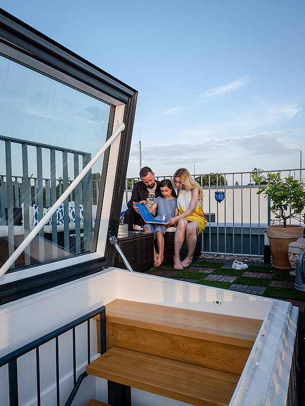 Familie sitzt auf der Dachterrasse eines Townhouses in Berlin, neben einem geöffneten Flachdach Ausstieg.