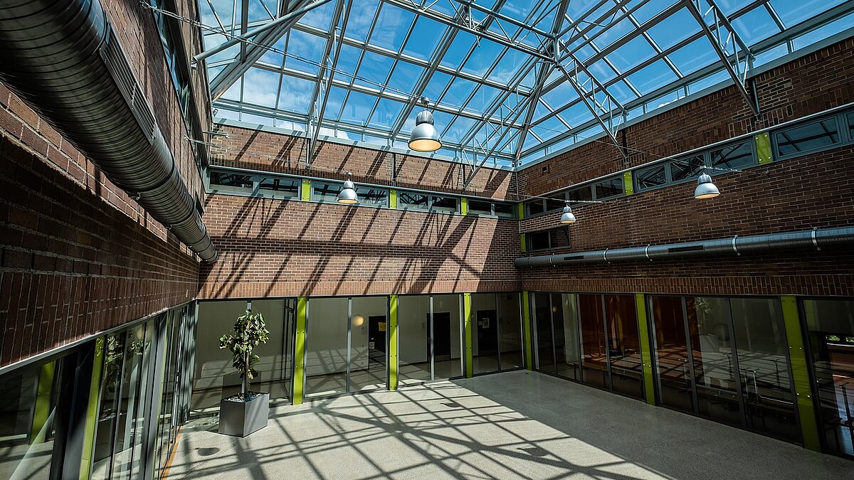 Innenansicht des Dante-Gymnasiums mit großem Glasdach, Stahlkonstruktion, Ziegelwänden und Lichtdurchflutung.