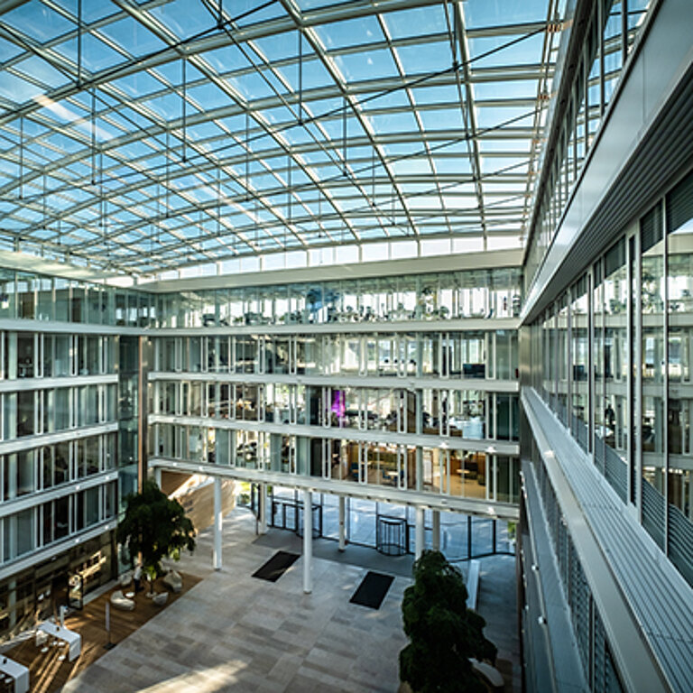 Großzügiges Atrium mit modernem Glasdach, das Tageslicht gleichmäßig über mehrere Geschosse verteilt und transparente Architektur erlebbar macht.