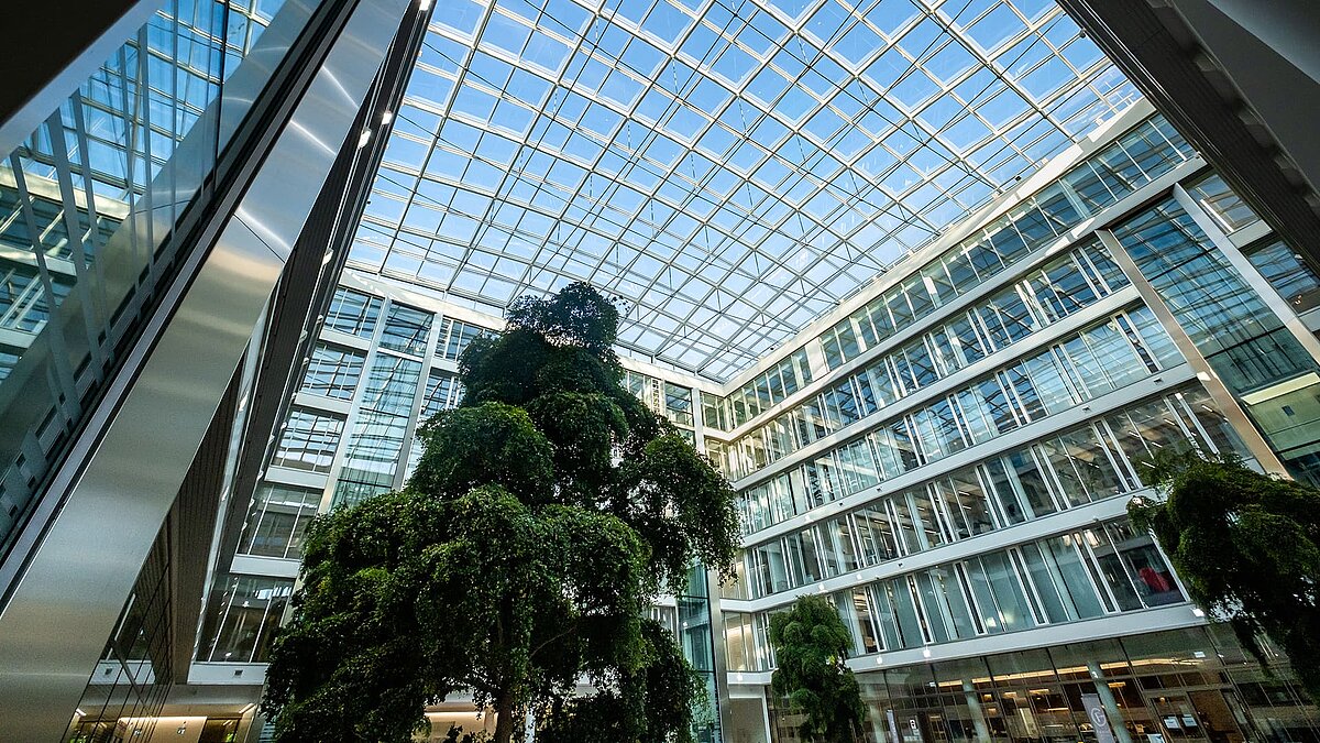 Innenansicht des Bürogebäudes Newton der TÜV Süd Gruppe mit Glasdach und großen Bäumen im Atrium.