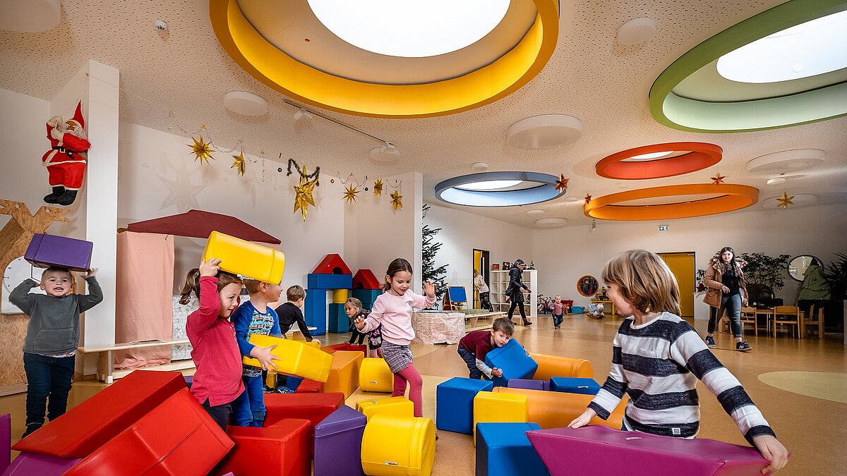Kinder spielen in der Kindertagesstätte Glückliche Zukunft in Sömmerda mit bunten Bausteinen unter farbigen, runden Deckenfenstern.