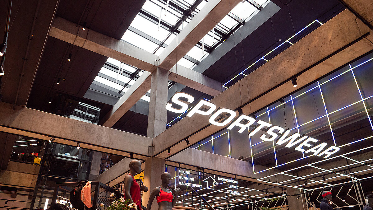 Leuchtender Sportswear Schriftzug im Vordergrund. Dahinter ein Glasdach