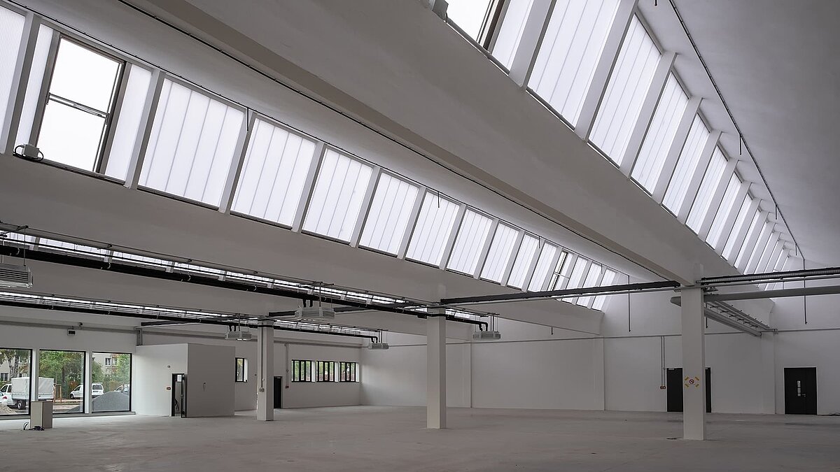 Innenansicht des alten Postbahnhofs Leipzig, saniert mit großen Lichtbändern und moderner weißer Architektur.