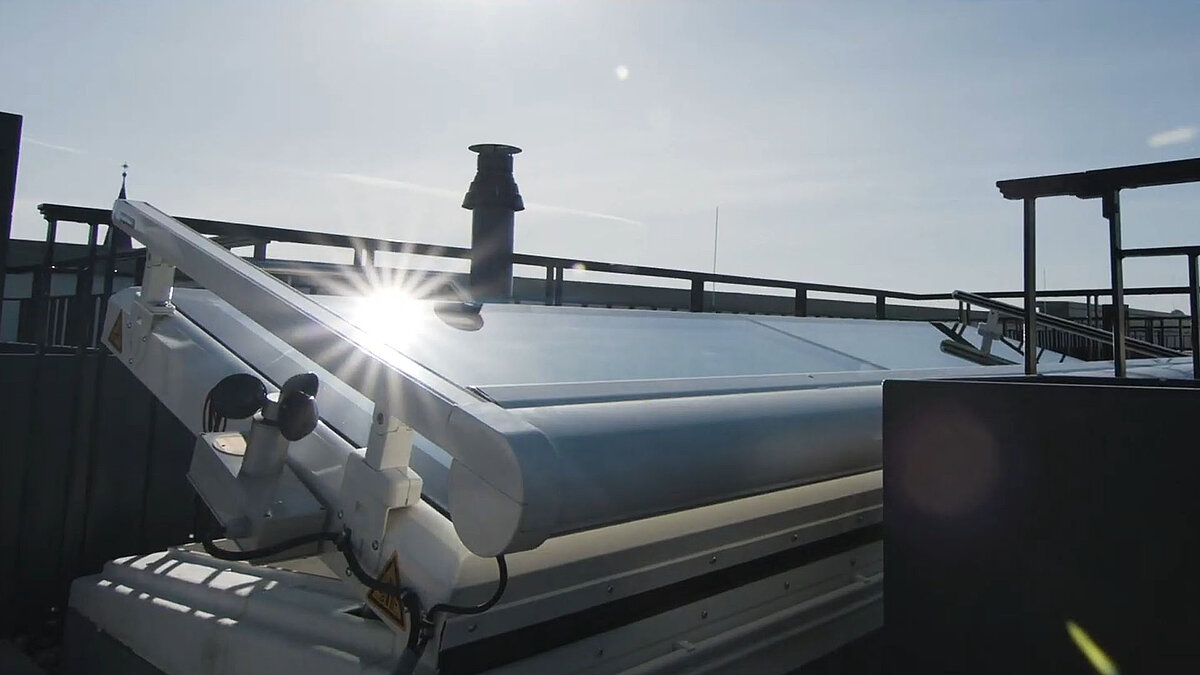 Geöffneter LAMILUX Flachdach Ausstieg mit Sonnenspiegelung auf der Glasfläche.