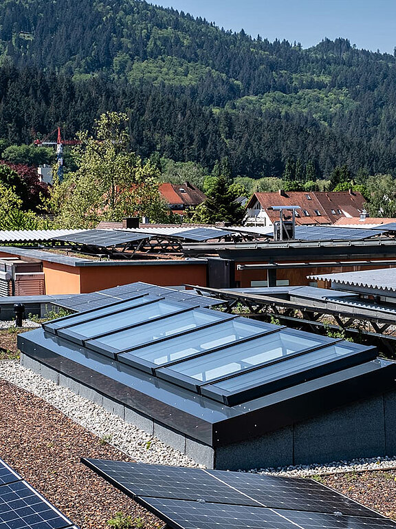 Dachansicht eines Wohnhauses in Freiburg mit modularen Glasdachfenstern von LAMILUX, eingebettet in eine Umgebung mit Solaranlagen und grüner Natur