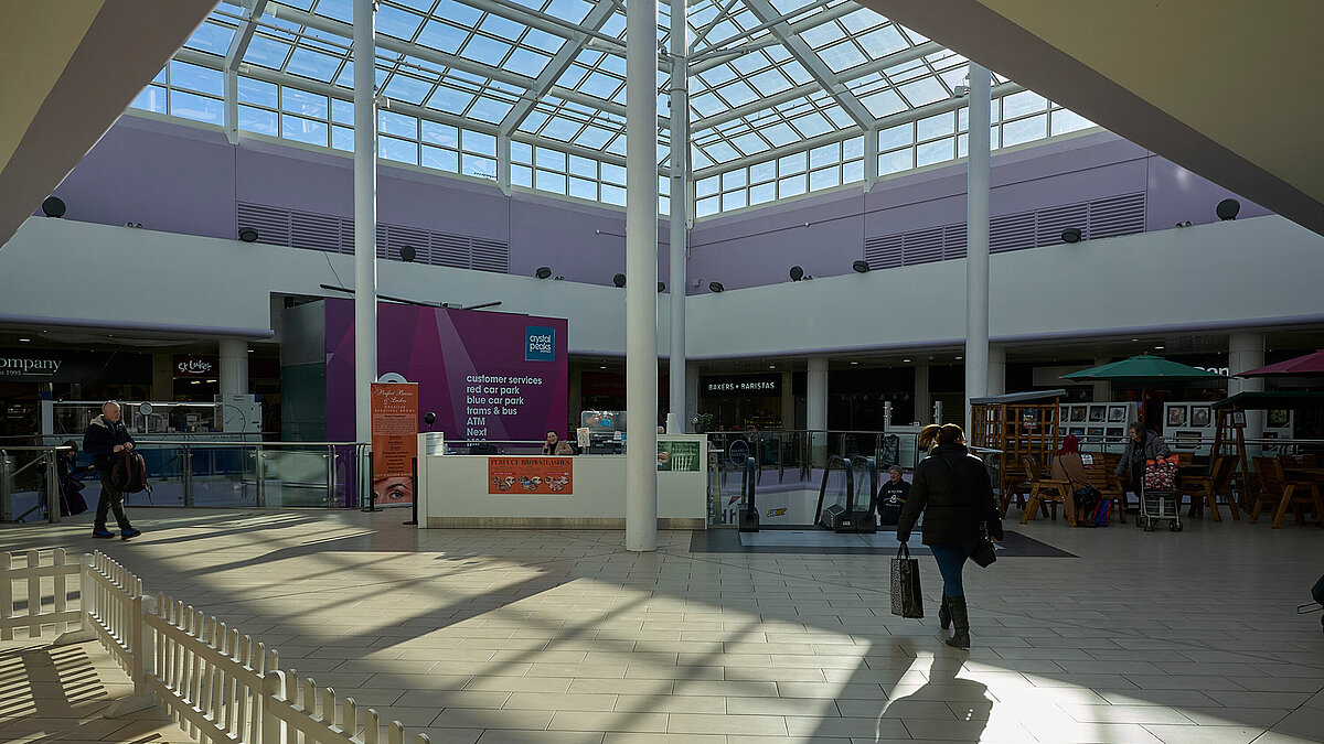 Innenraum eines Einkaufszentrums mit Glasdach und Sonnenschein, Menschen gehen und kaufen ein