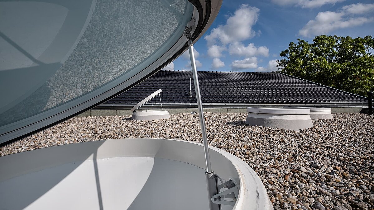 Offenes Oberlicht auf dem Kiesdach der Kindertagesstätte Sonnenfeld in Wandlitz bei blauem Himmel und weißen Wolken.