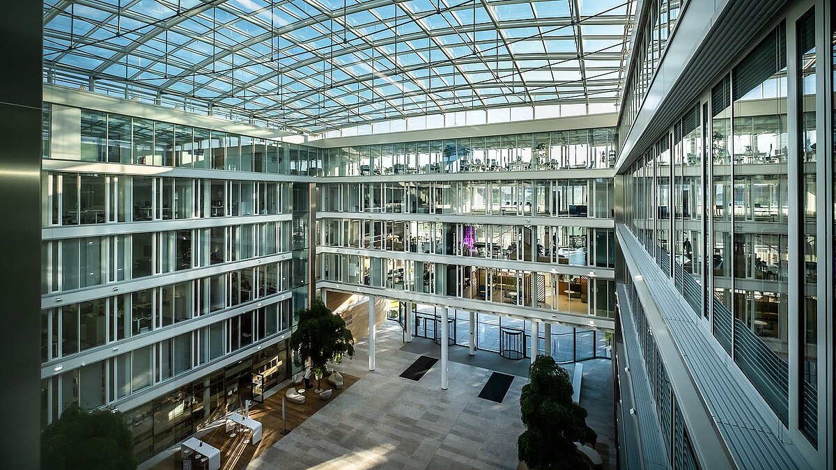 Modernes Atrium des Bürogebäudes Newton der TÜV Süd Gruppe mit Glasdach und großen Glasfassaden.