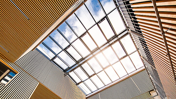 Architektonisch auffälliges Glasdach mit wellenförmigen Holzelementen und Sonnenlicht.