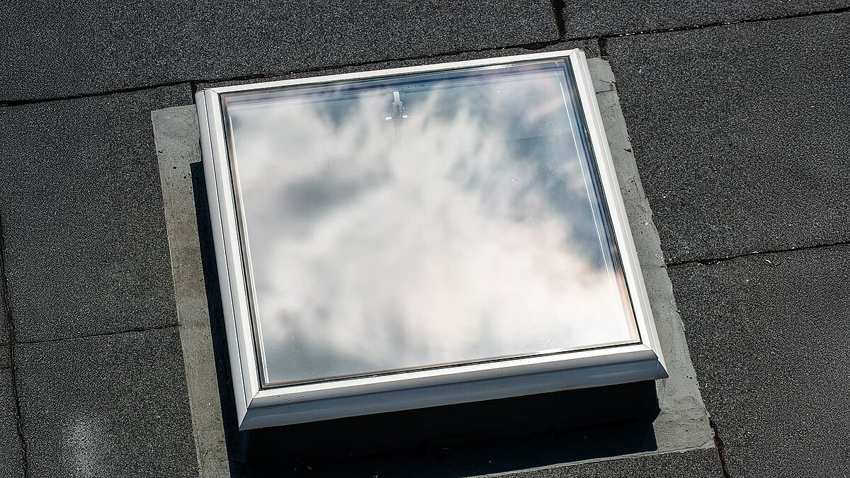 Geschlossenes Flachdach-Fenster mit Spiegelung des Himmels auf einem grauen Dach der Caritas Hagen.