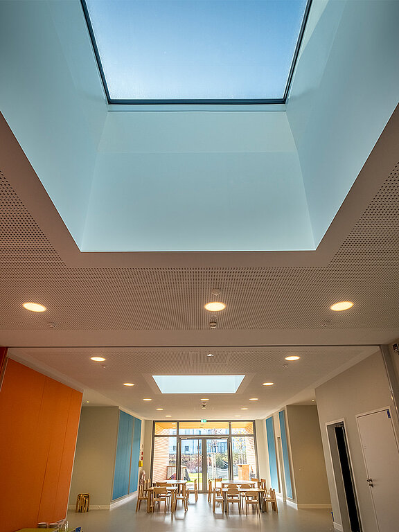 Heller Raum mit großem Glas-Oberlicht, bunten Wänden und Kindermobiliar