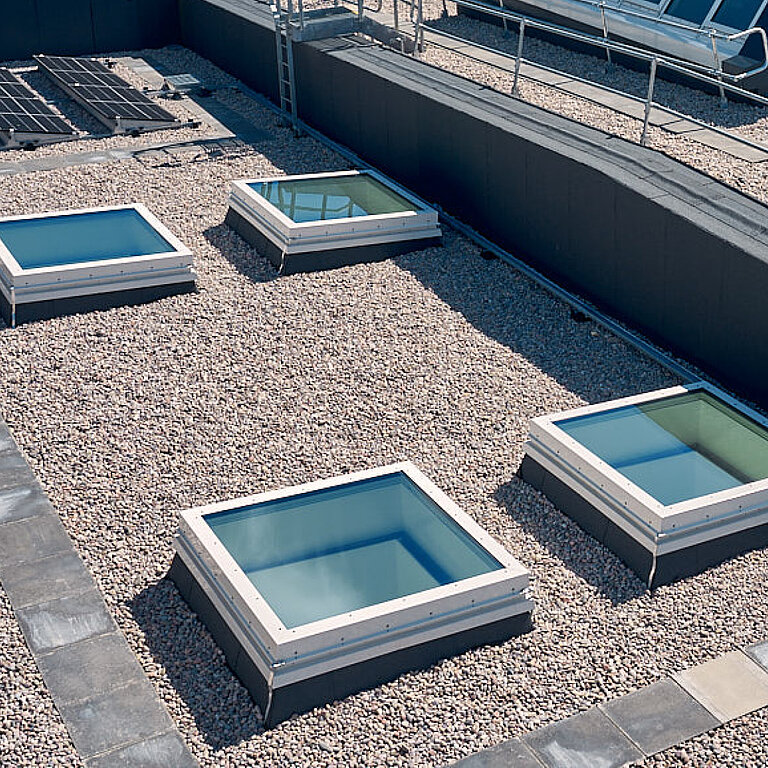 Flachdach Fenster FE Passivhaus+ auf einem Flachdach mit mehreren rechteckigen Dachfenstern zur energieeffizienten Tageslichtnutzung.