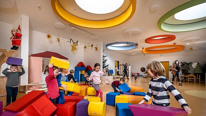 Kita-Kinder spielen unter bunten Tageslichtelementen Runde Flachdach Fenster mit bunter Verkleidung in der Kita Glückliche Zukunft in Sömmerda | insights by LAMILUX