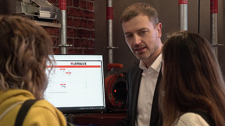 Bauingenieur Carsten Ficker erklärt LAMILUX Produktkonfigurator Carsten Ficker Leiter LAMILUX Academy auf digitalBAU mit zwei Messestandsbesucherinnen | insights by LAMILUX