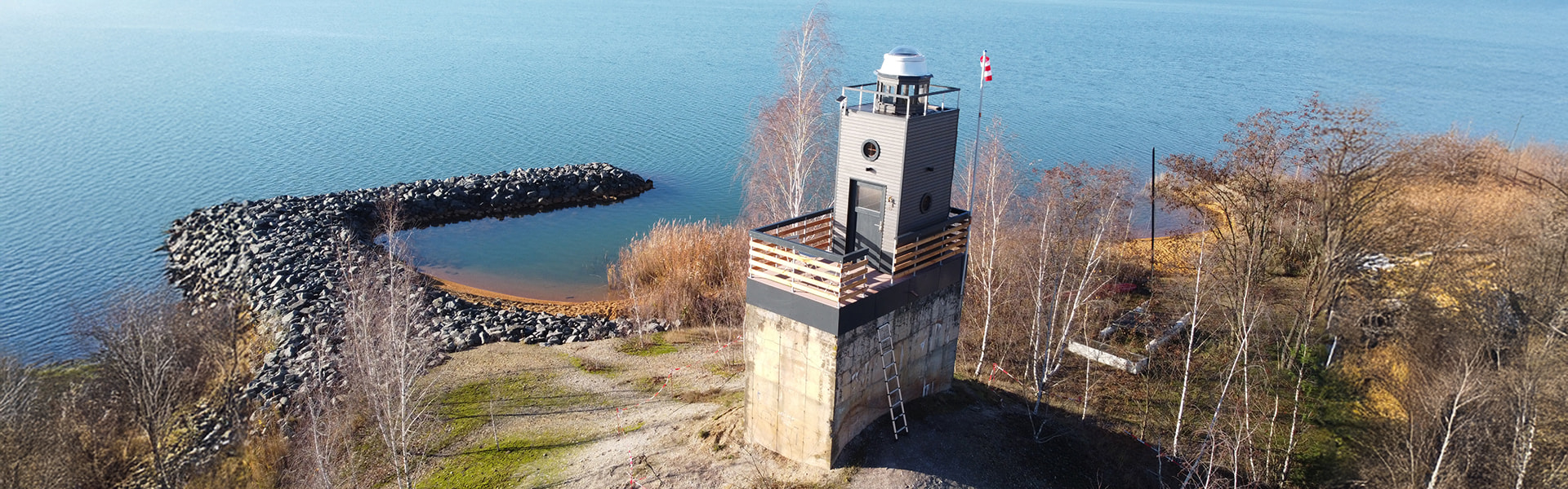 Leuchtturm am Seeufer mit umliegender Natur und Blick auf das Wasser.