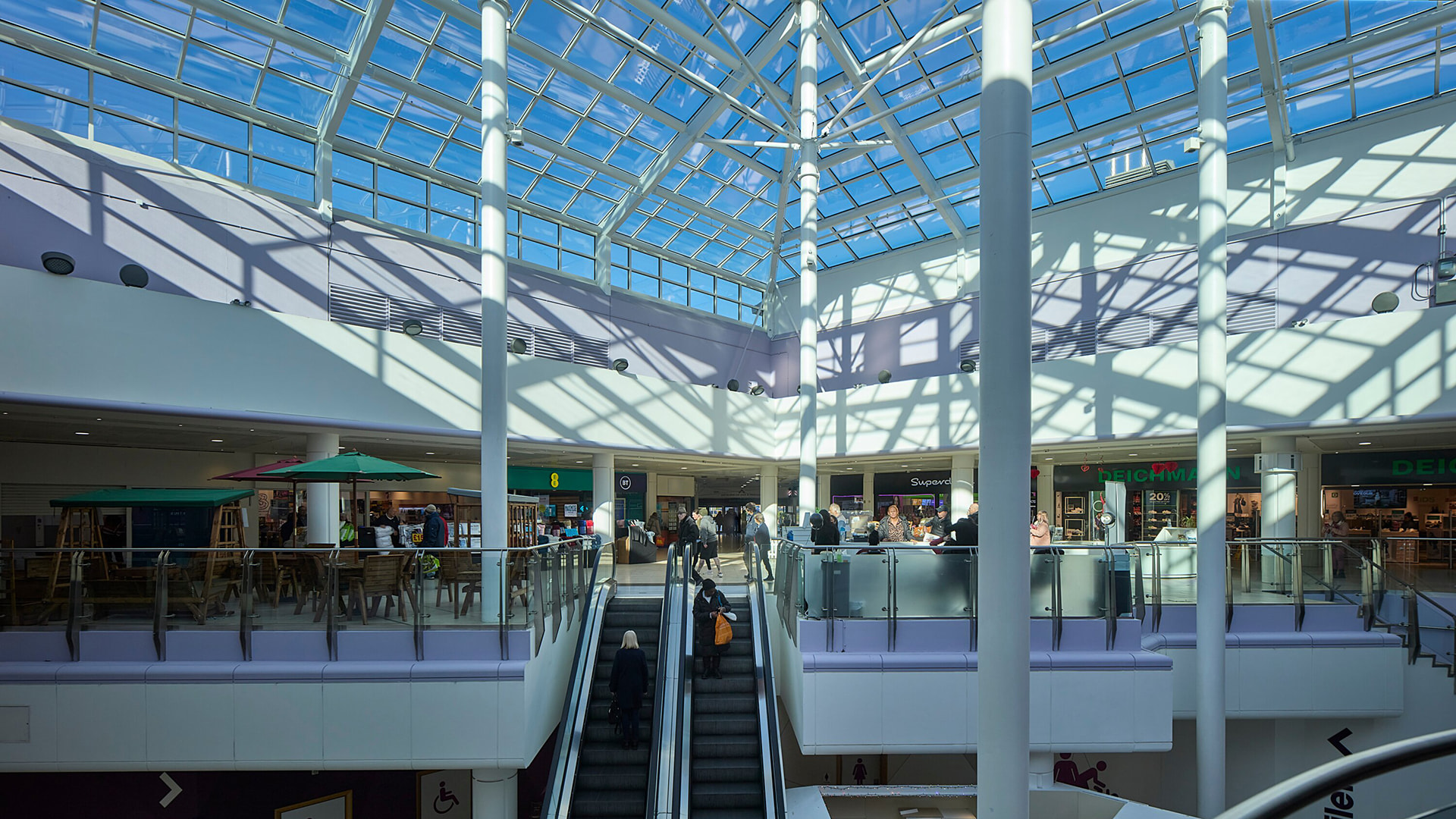 Einkaufszentrum mit Glasdach, zwei Ebenen und Menschen, die die Rolltreppe benutzen