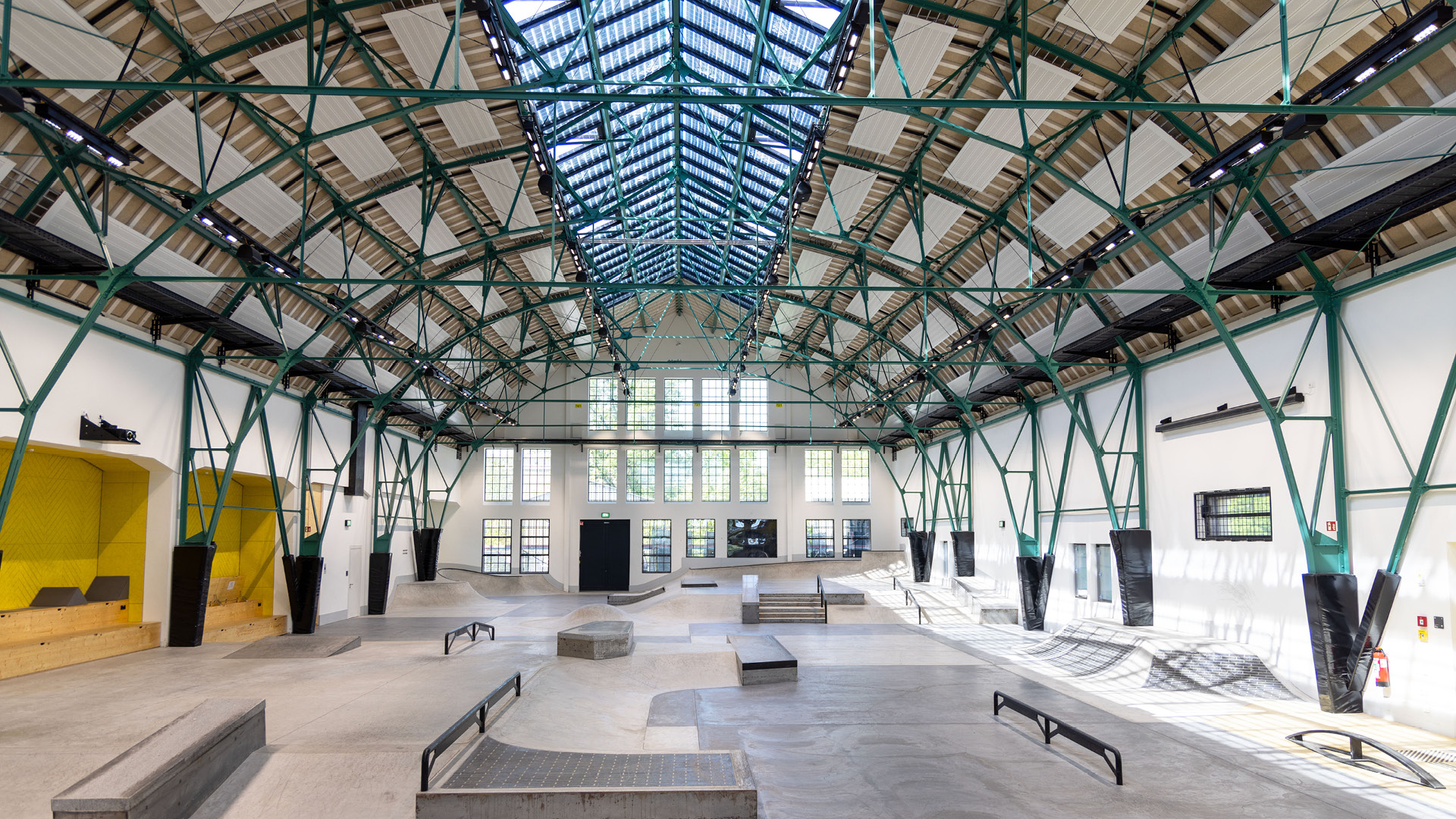 Große Skaterhalle mit Rampen und Fahrflächen unter weitspannender Stahlkonstruktion und durchgehendem Glasdach für natürlichen Tageslichteinfall